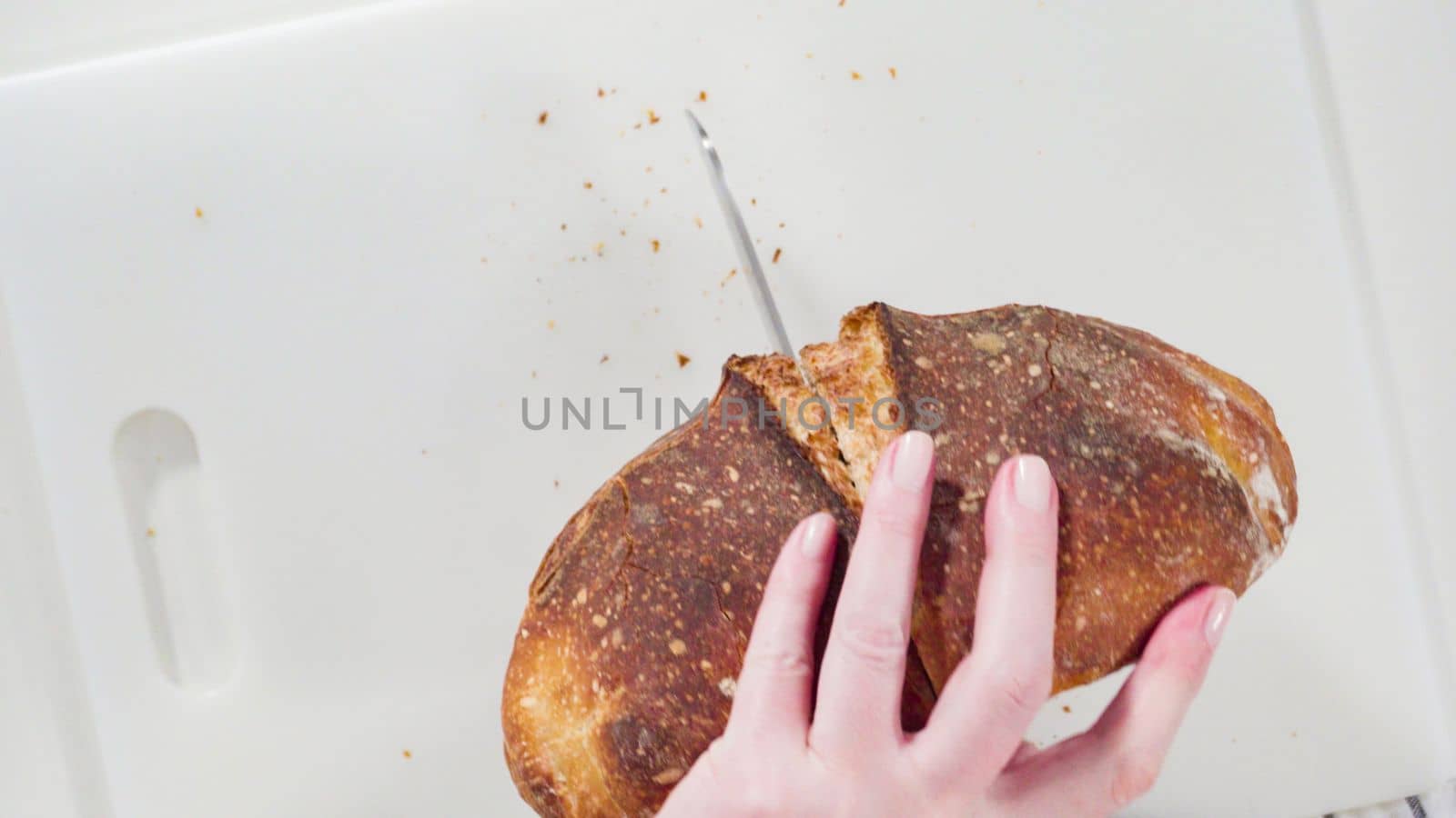Flat lay. Slicing freshly baked sourdough wheat bread on a white cutting board.