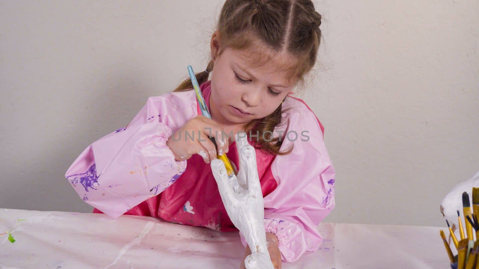 Little girl painting paper mache figurine at homeschooling art class.