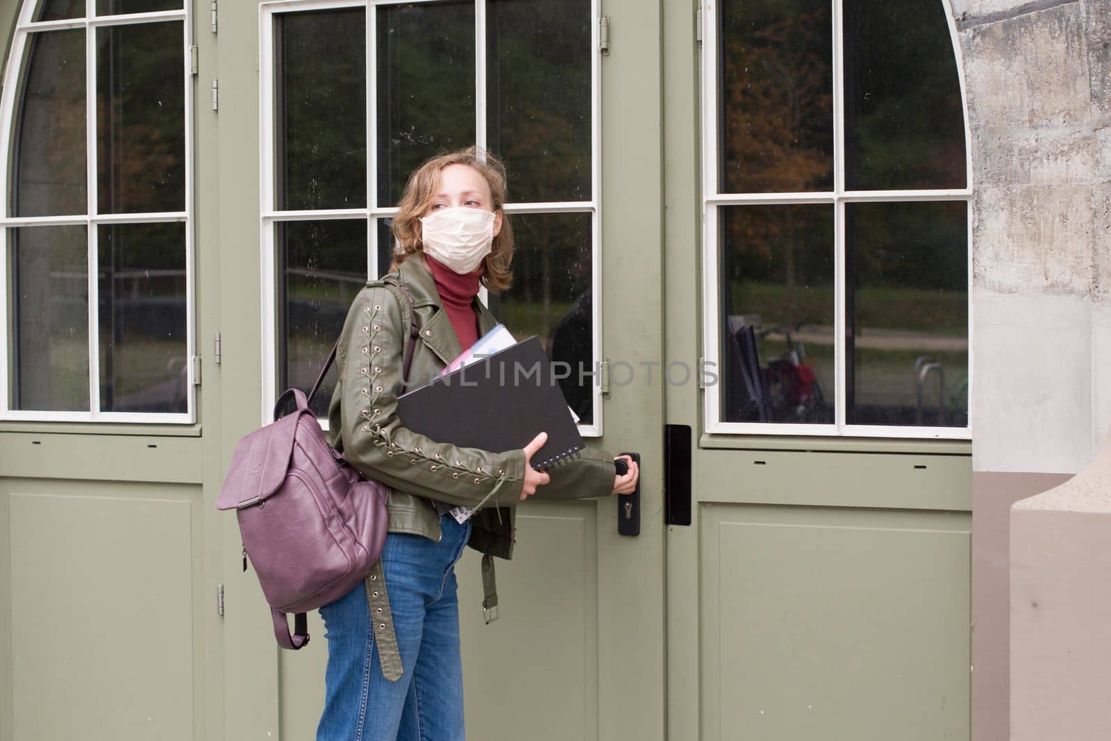 female student in a protective mask holds notes and opens the door to the collegeHigh quality photo