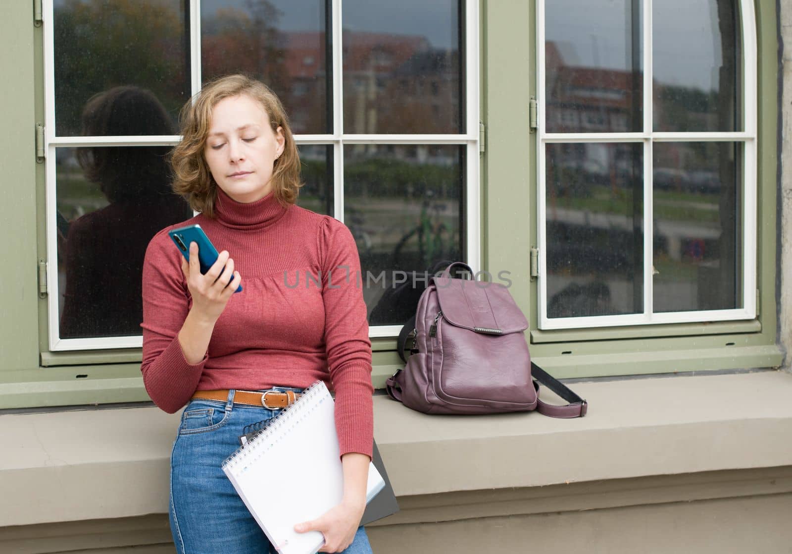 anxious girl student waiting for someone near college and reading messages on smartphone, back to school, High quality photo
