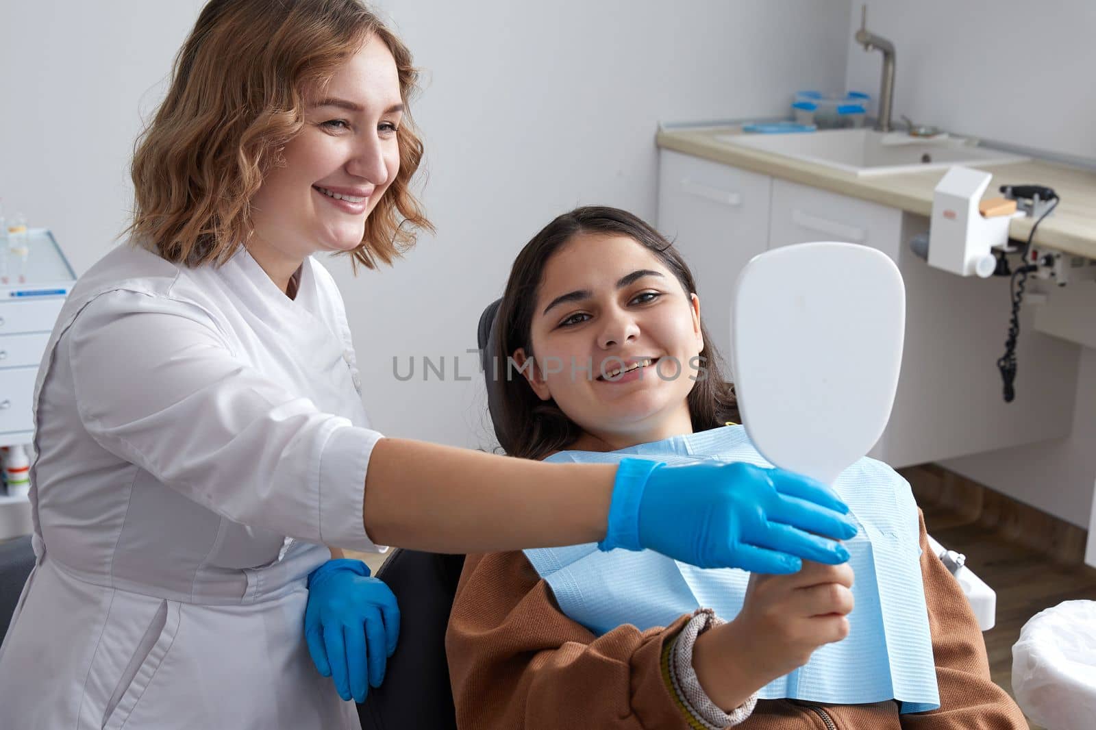 Young Woman checking her beautiful smile in mirror after stomatological treatment by Mariakray