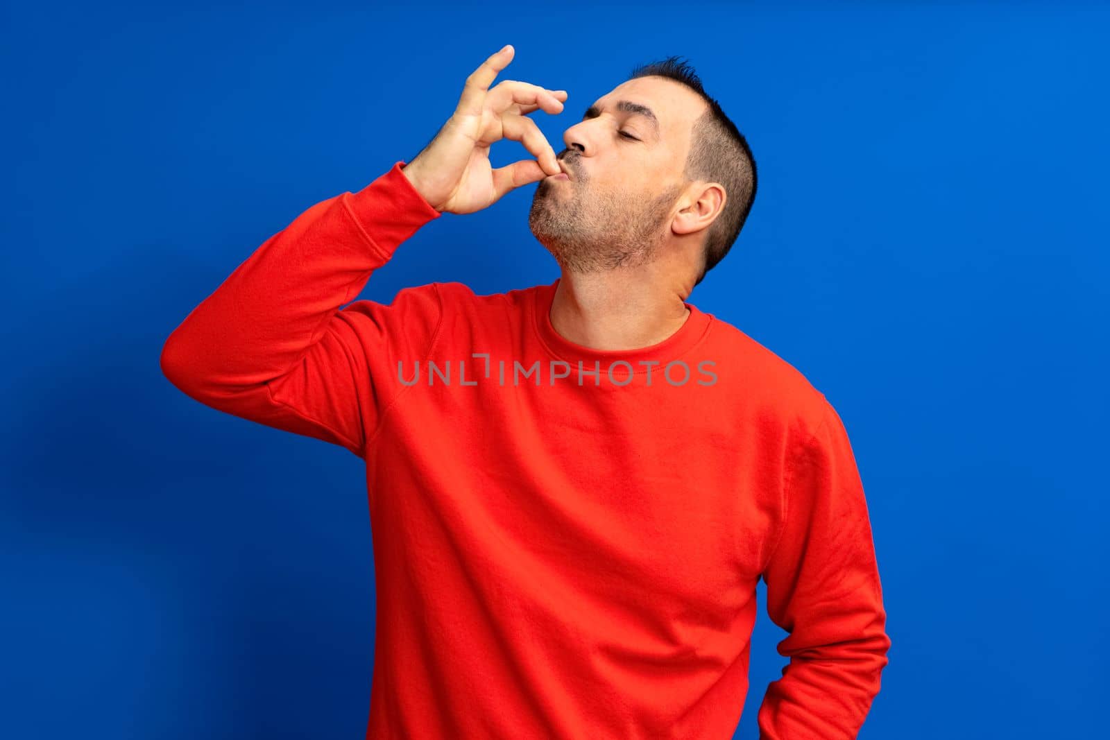 Photo portrait of a man with pursed lips showing gourmet sign with fingers tasty delicious isolated on blue colored background