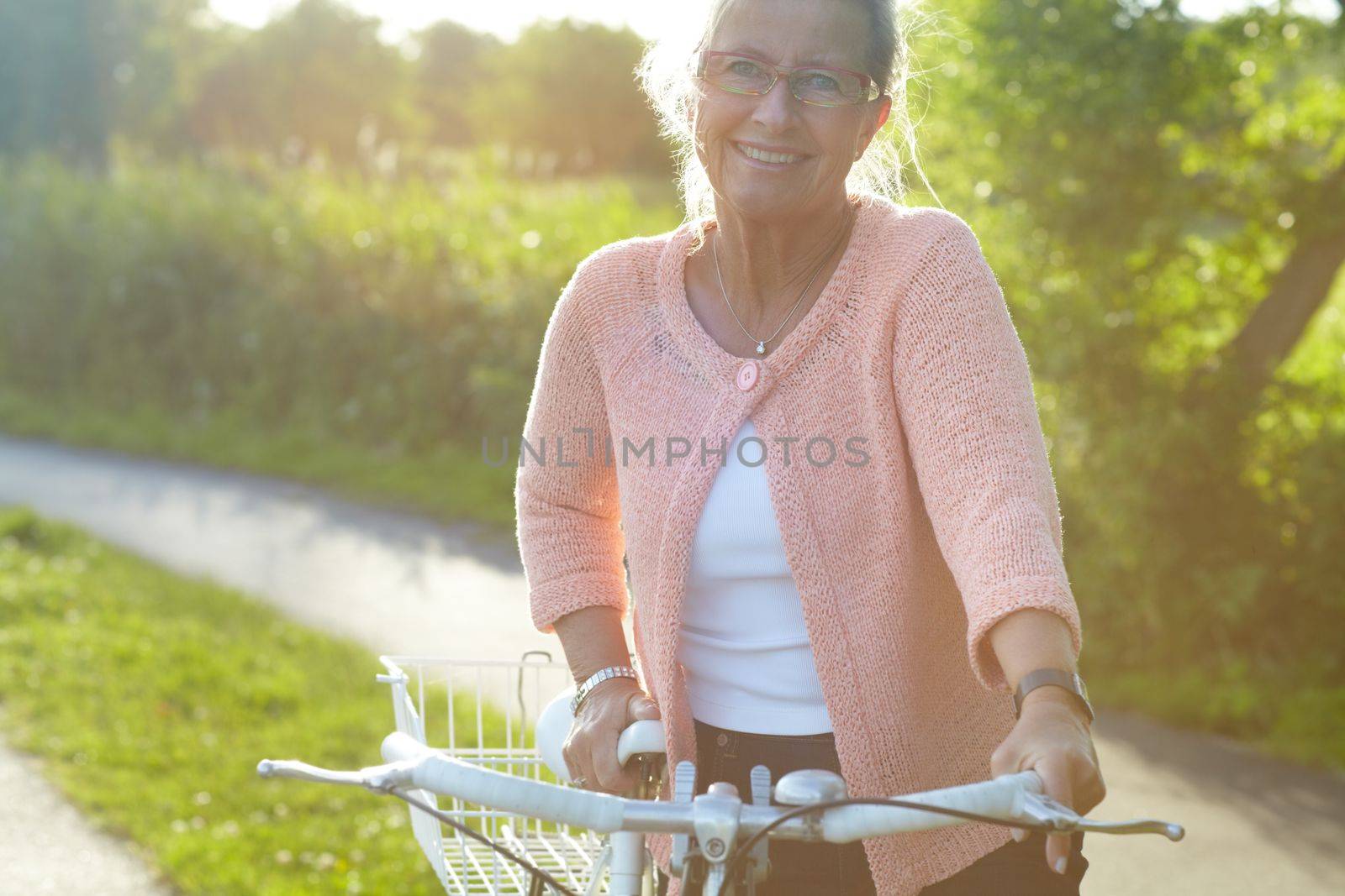 Summer biking. A lovely senior woman standing with her bike beneath a summer sun. by YuriArcurs