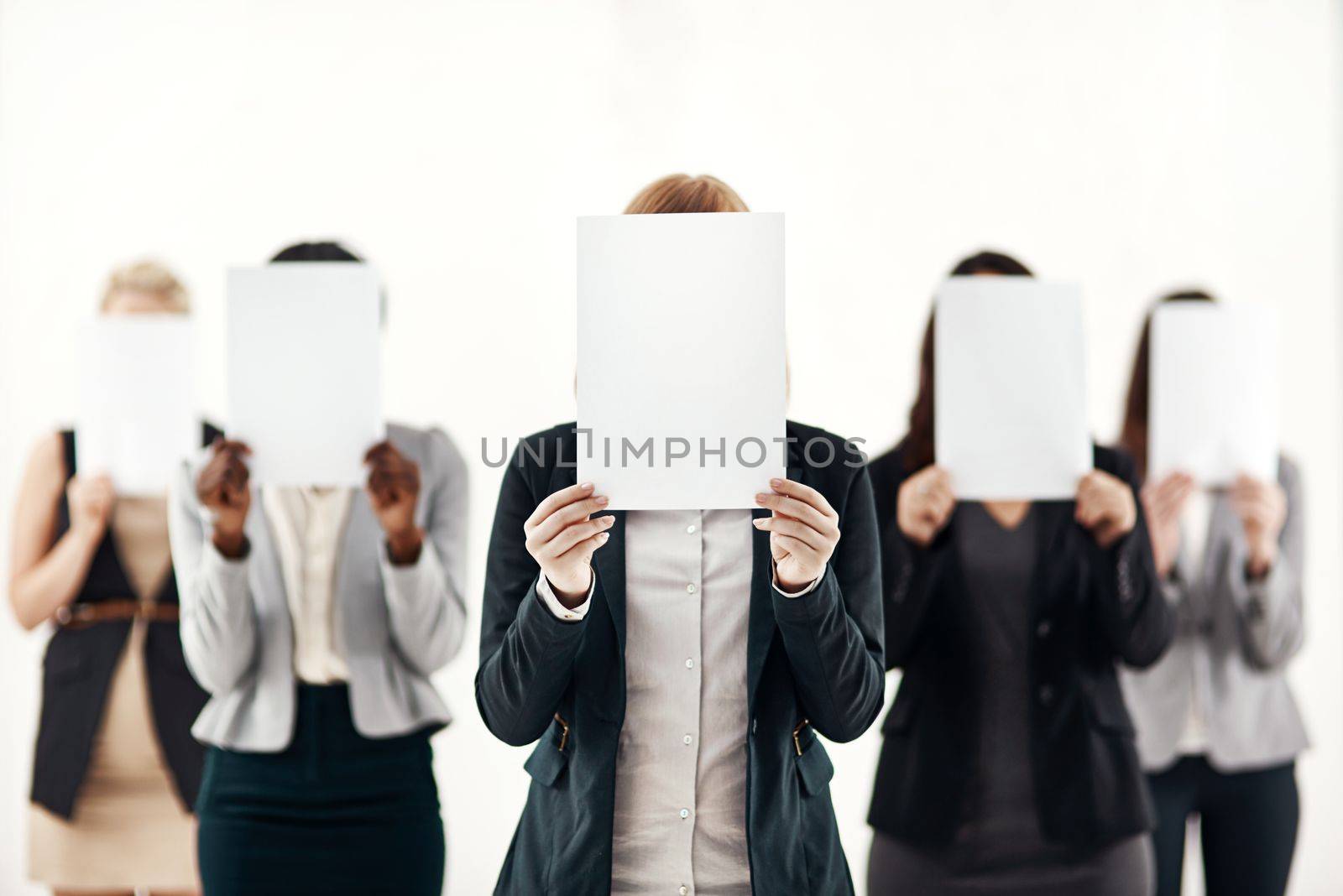 They each have something to say. a group of unrecognizable businesspeople holding blank pieces of paper over their faces against a white background. by YuriArcurs