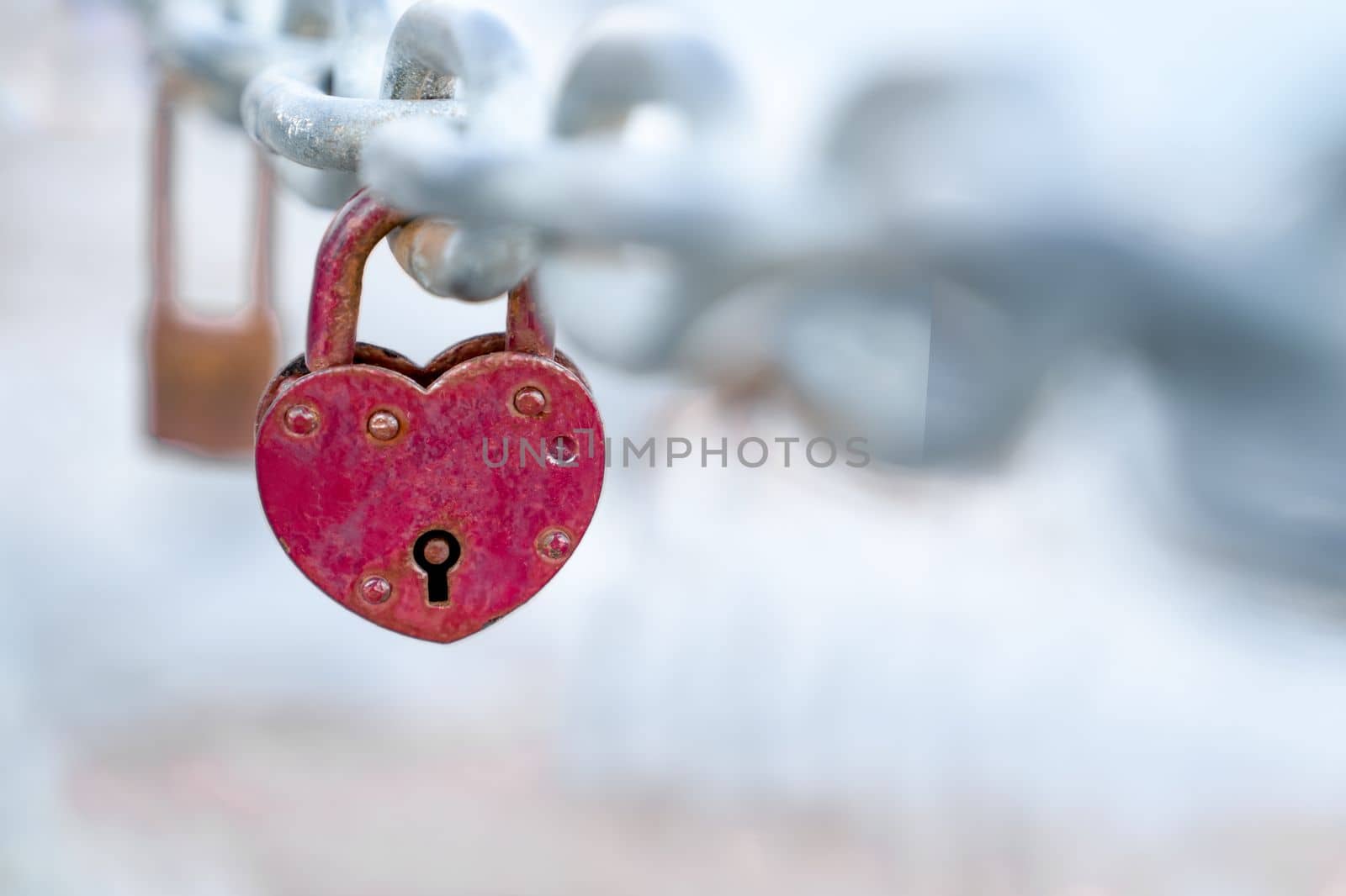 Red heart shaped lock hangs from bridge chain, wedding custom is symbol of eternal love, copy space