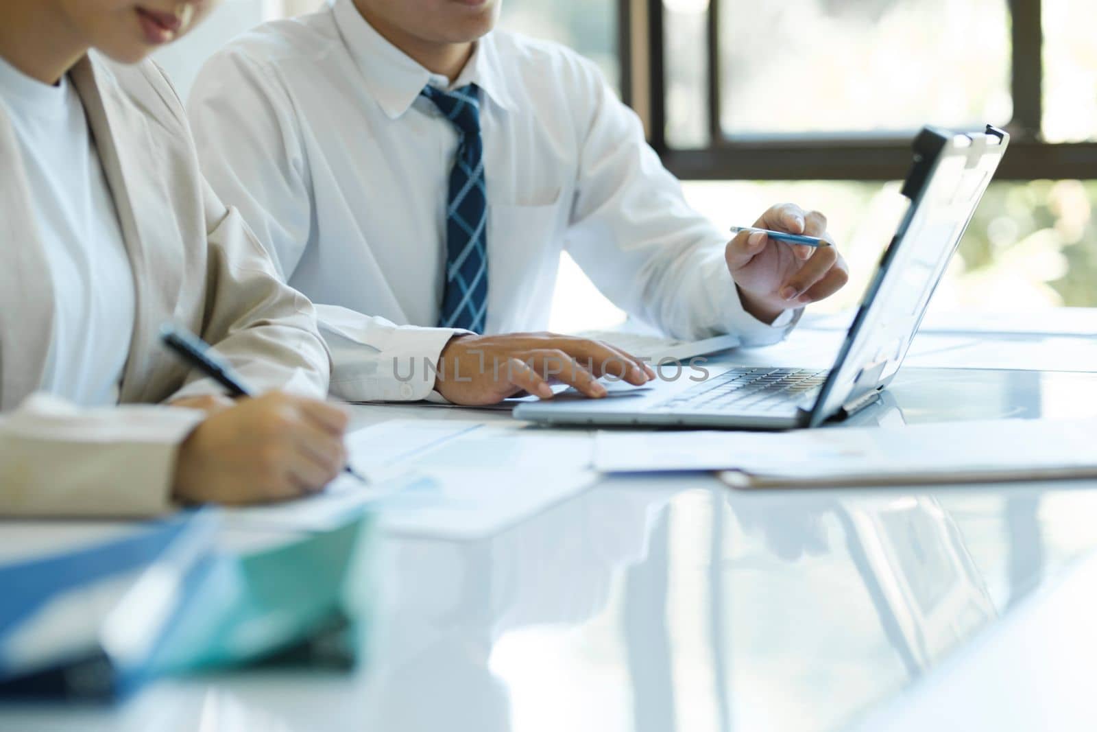 Close up businesspeople or colleagues are working together on investment project, discussing, sharing ideas, planning, and analyzing the business strategy and finance using laptop and graphs at workplace.