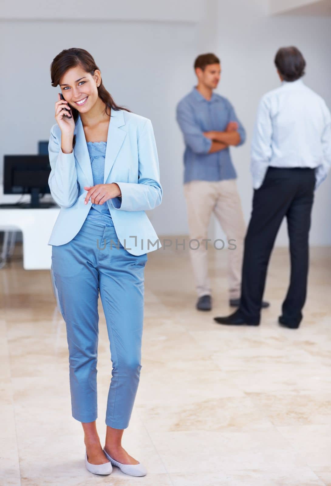 Female executive on call. Full length of successful young woman on call with business people discussing in background. by YuriArcurs
