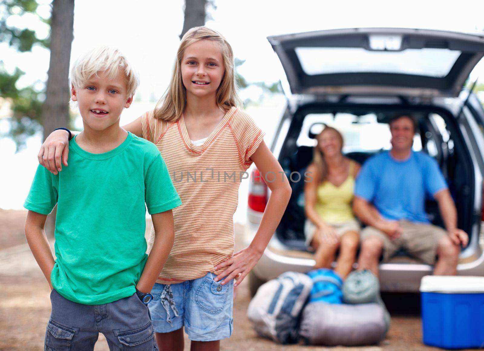Family enjoying vacation. Portrait of young brother and sister enjoying their vacation with parents sitting in the back of a car