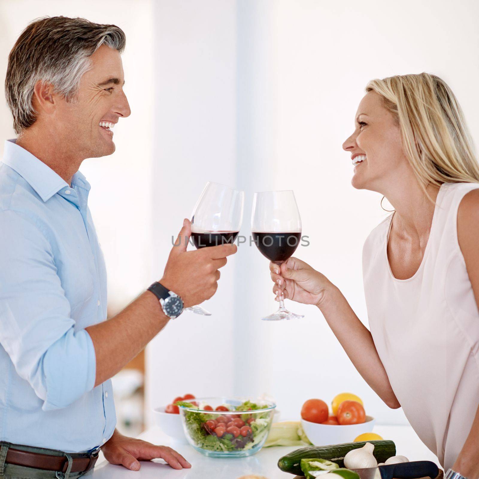 Cheers, babe. an affectionate mature couple toasting with red wine while making dinner. by YuriArcurs