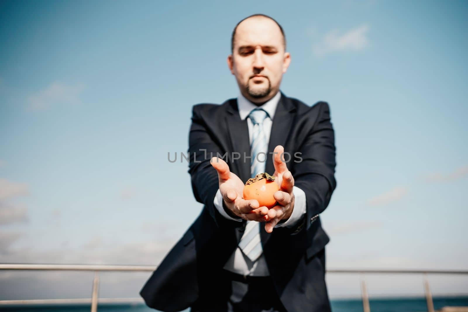 Male persimmon park. Hipster millennial man in a tie and jacket bites off a persimmon while sitting on a park bench in slow motion Young business people eat golden persimmons at lunchtime
