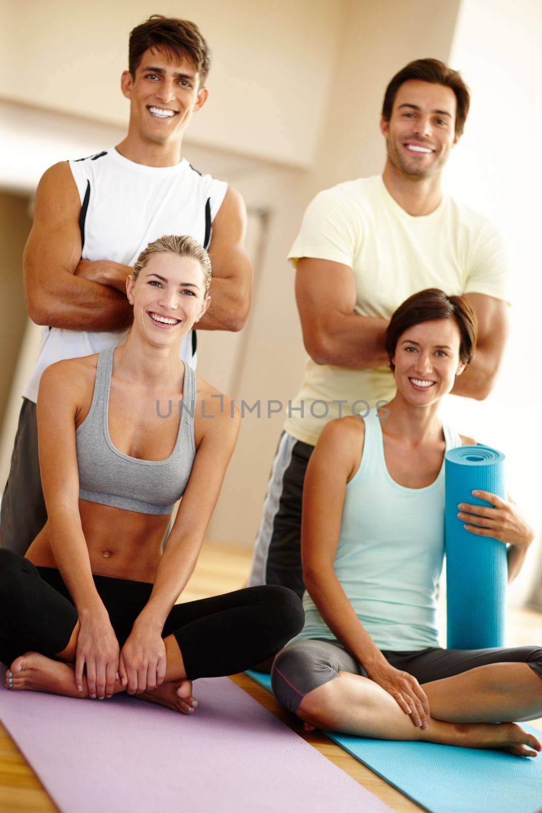 Yoga for everyone. Portrait of four young adults smiling at the camera with their yoga gear. by YuriArcurs