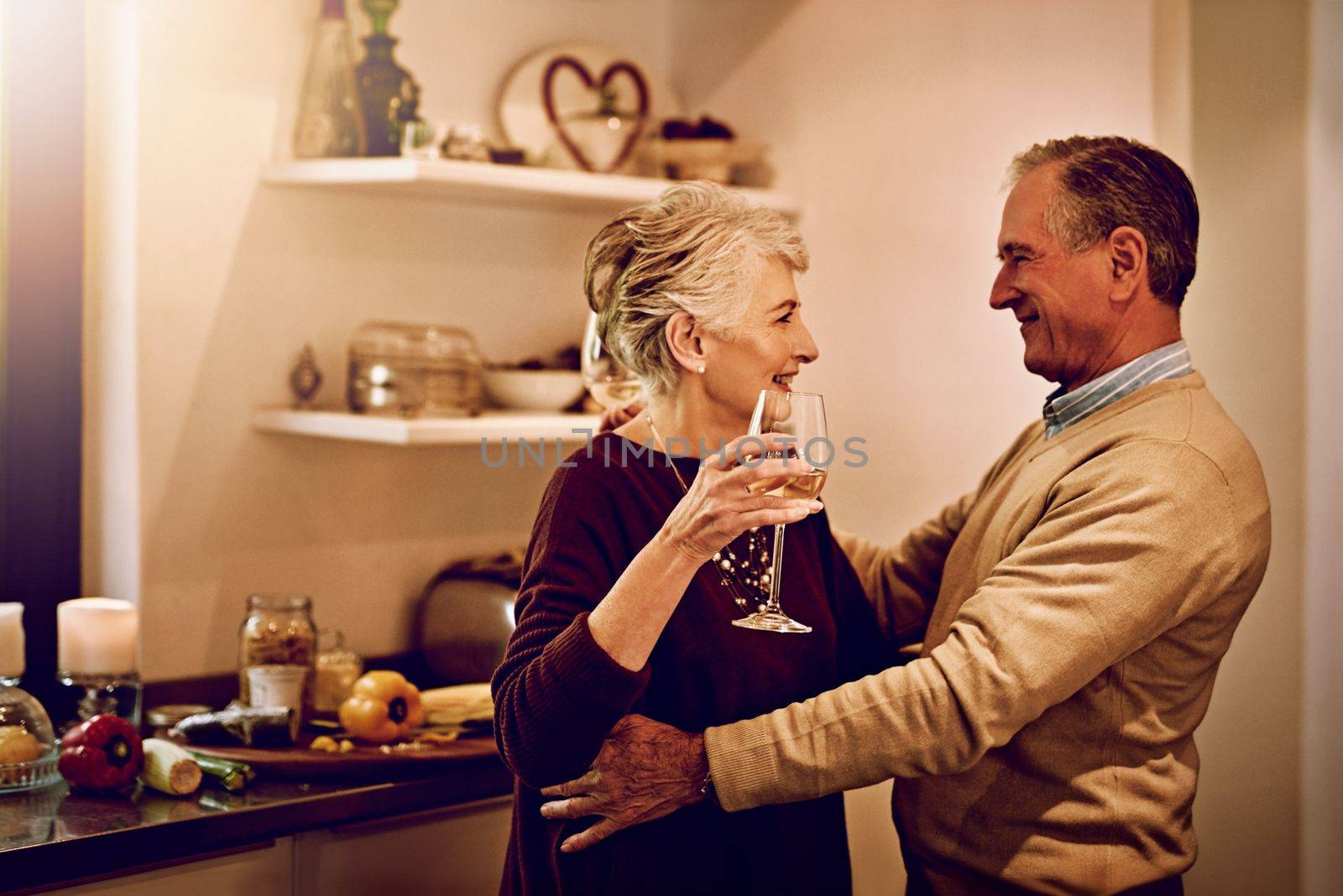 True romance doesnt fade with time. an elderly couple dancing with each other in their kitchen. by YuriArcurs