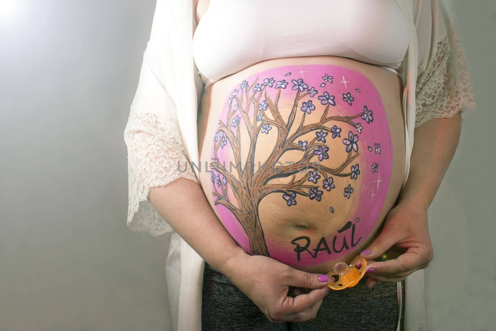 Eight month pregnant woman holding a pacifier in orange color