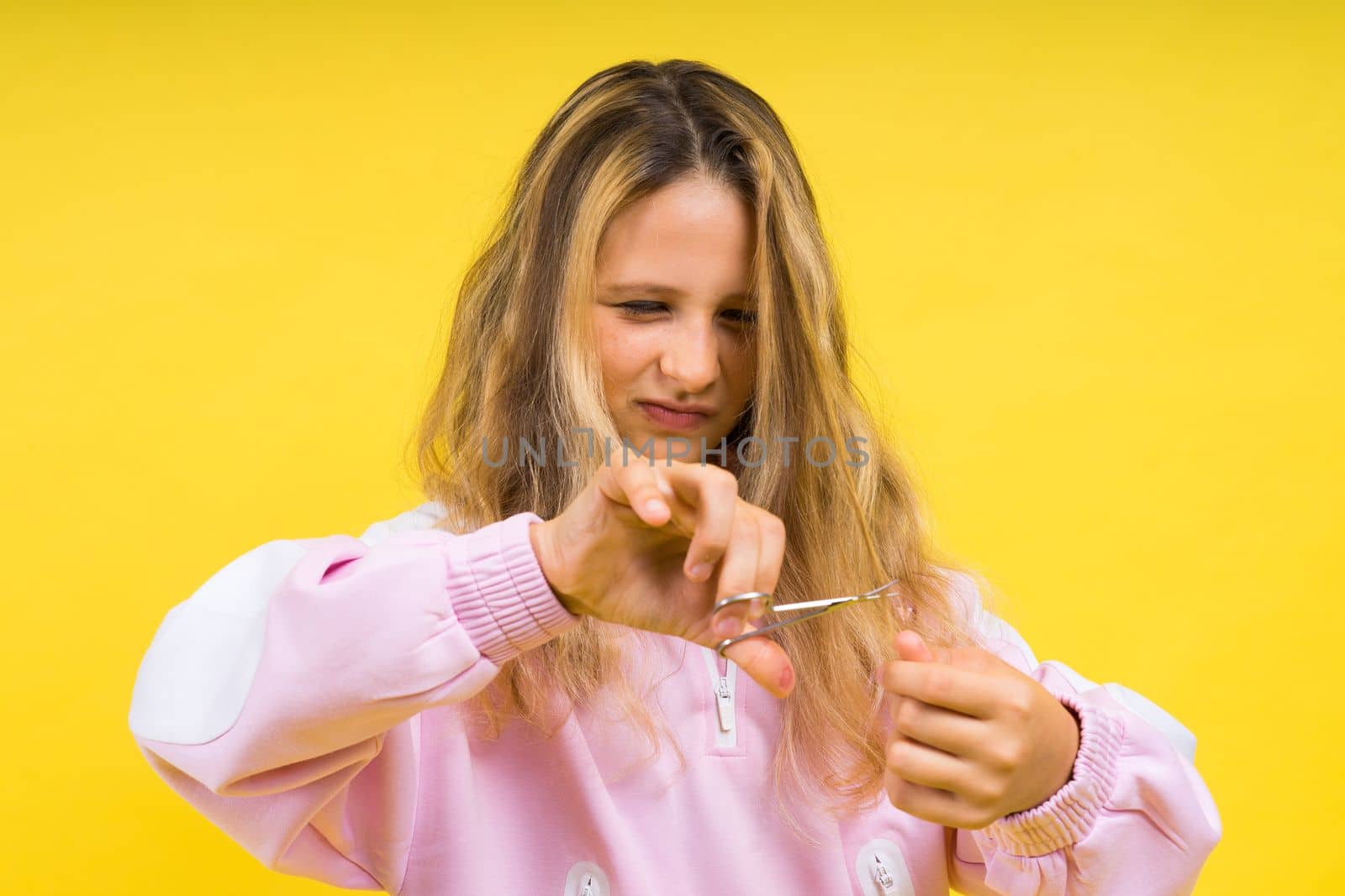 Child adorable girl hairdresser cutting long blonde hair with metallic scissors on yellow by Zelenin
