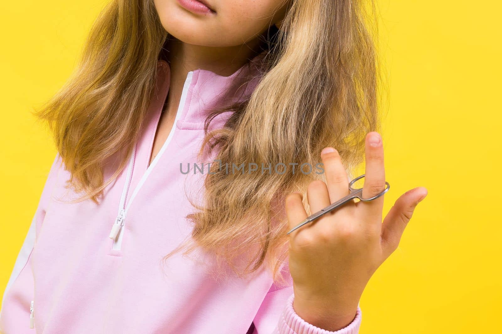 Child adorable girl hairdresser cutting long blonde hair with metallic scissors on yellow by Zelenin