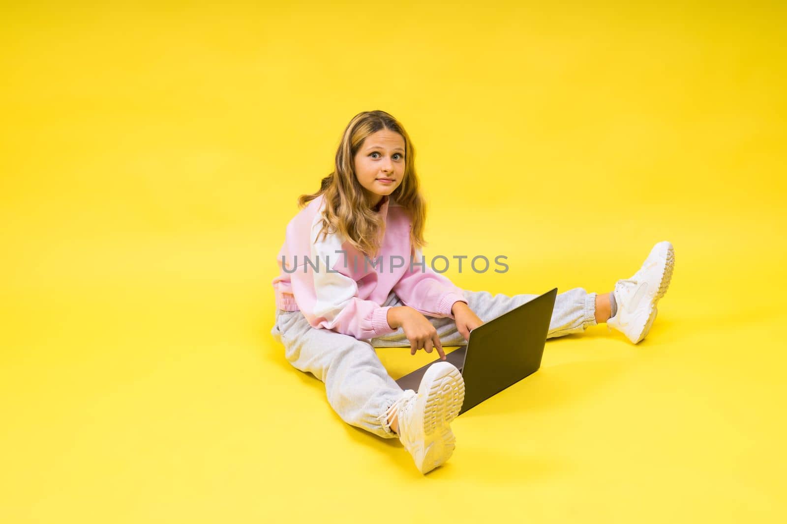 Beautiful little girl sitting on a light floor with a gray laptop and smiling, empty space by Zelenin