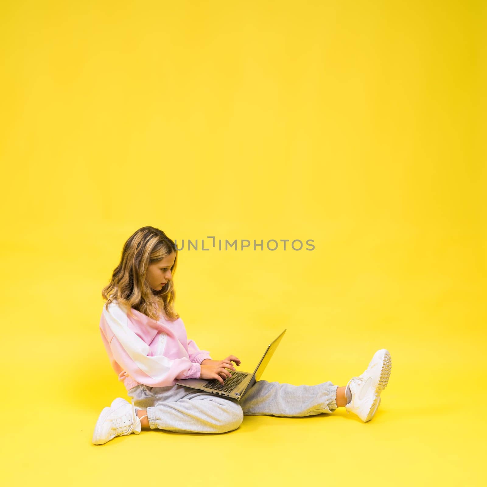 Beautiful little girl sitting on light floor with a gray laptop and smiling, empty space