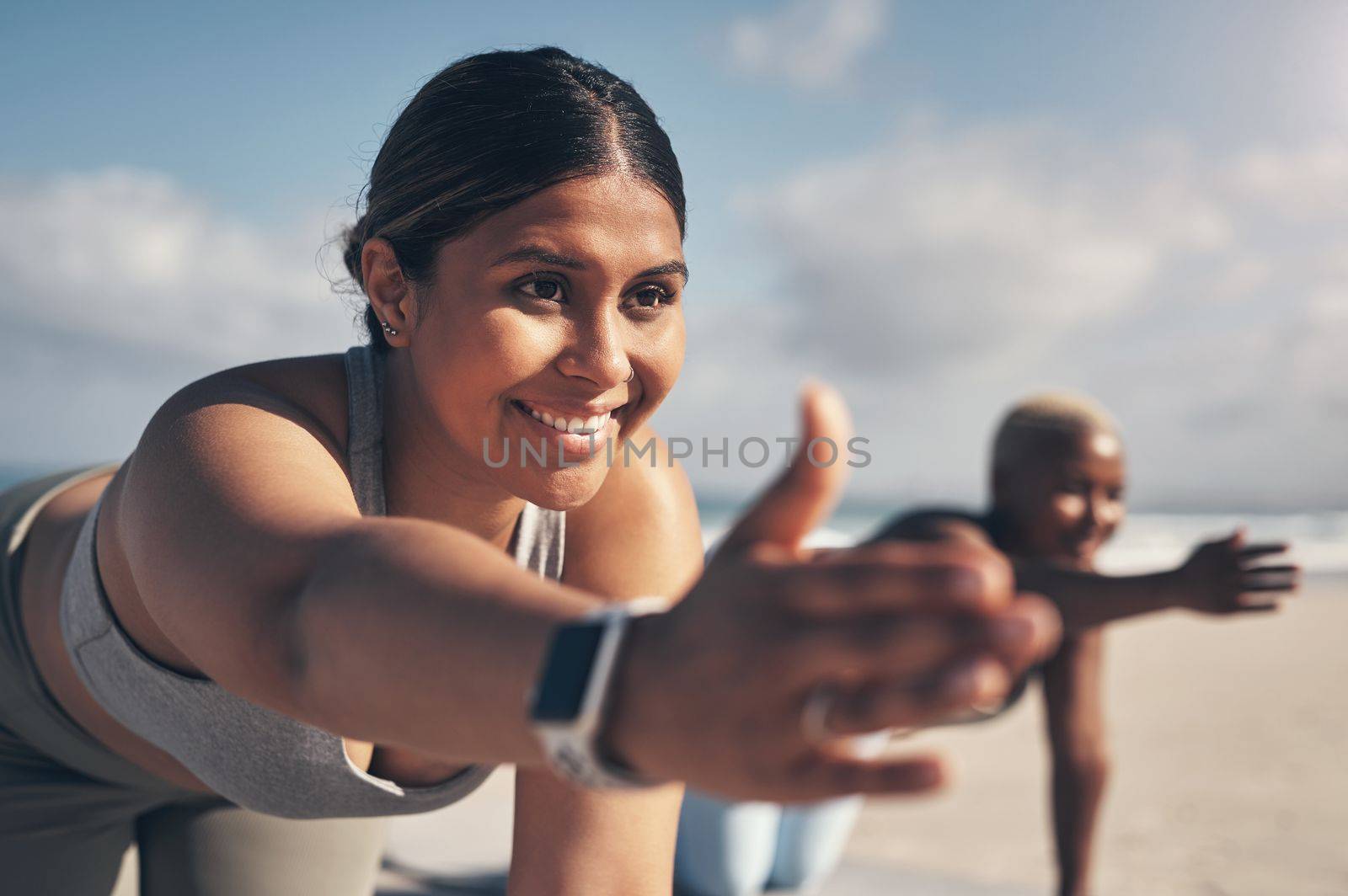 Yoga brings balance into my life. a young woman wearing a smartwatch while practicing yoga at the beach. by YuriArcurs