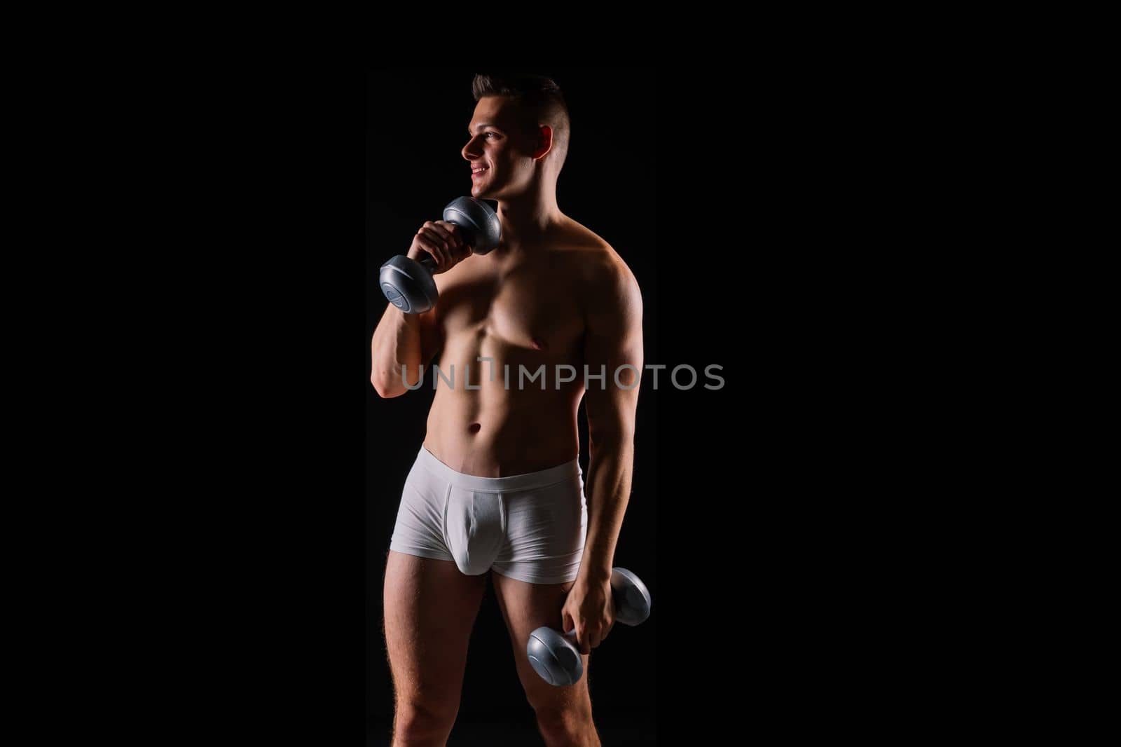 Shirtless bodybuilder holding a dumbell and showing his muscular arms.