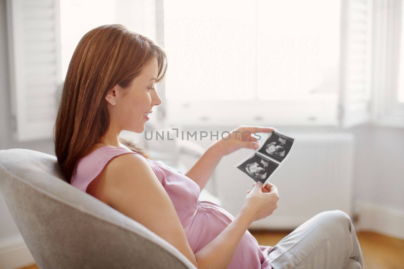 Looking at a glimpse of the future. Pretty young woman looking at her babies sonogram while sitting at home