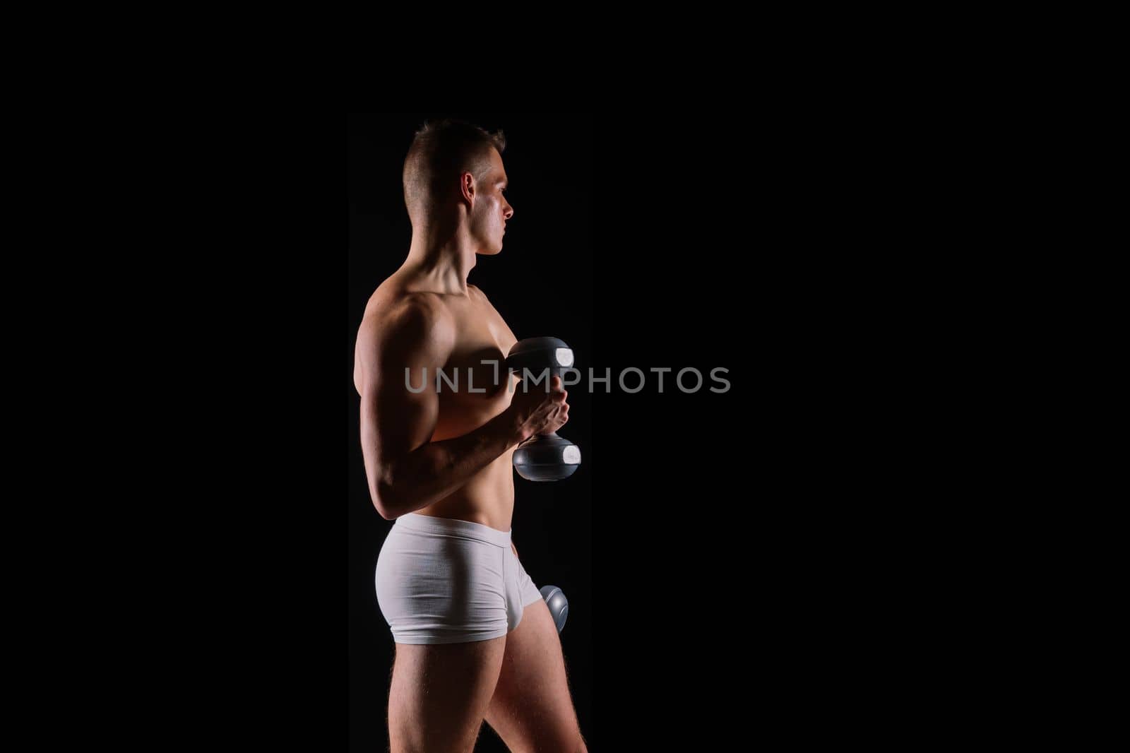 Shirtless bodybuilder holding a dumbell and showing his muscular arms.