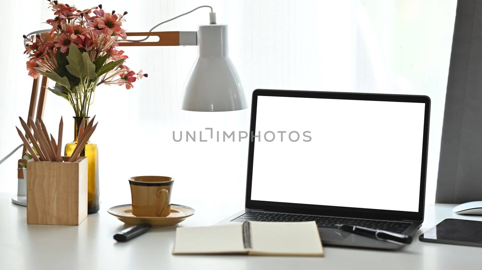 Feminine workplace with laptop computer cup of tea, pencil holder and flower pot on white table by prathanchorruangsak