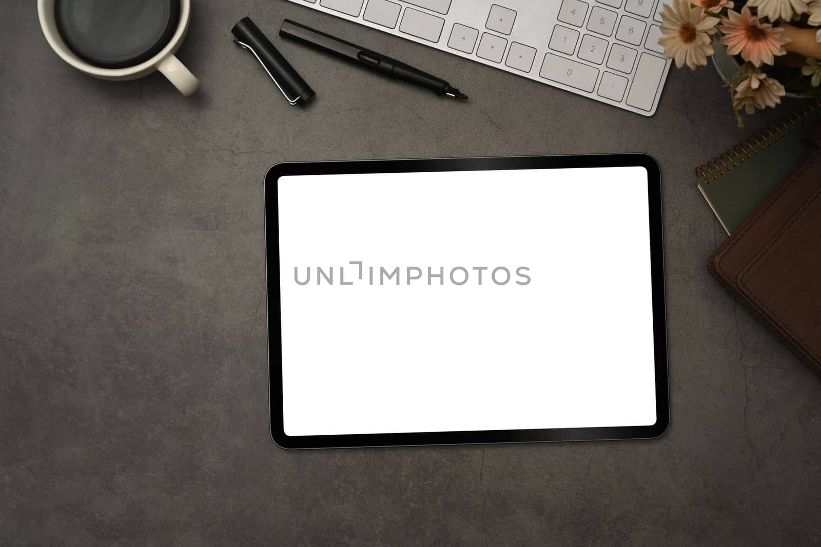 Top view of digital tablet with blank screen, cup of coffee and notepad on black slate texture background.
