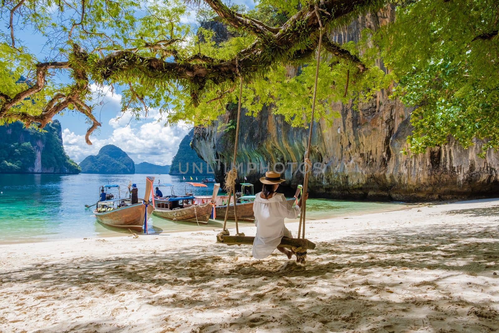 women on a swing at the Tropical lagoon of Koh Loa Lading Krabi Thailand part of the Koh Hong Islands in Thailand. beautiful beach with limestone cliffs and longtail boats