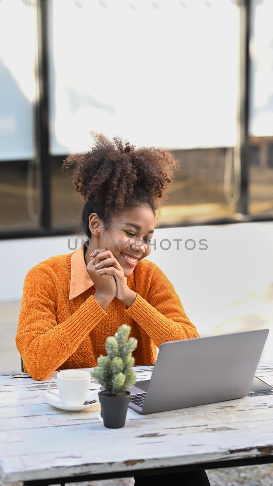 Cheerful African American woman sitting outdoor cafe and making video call on laptop.