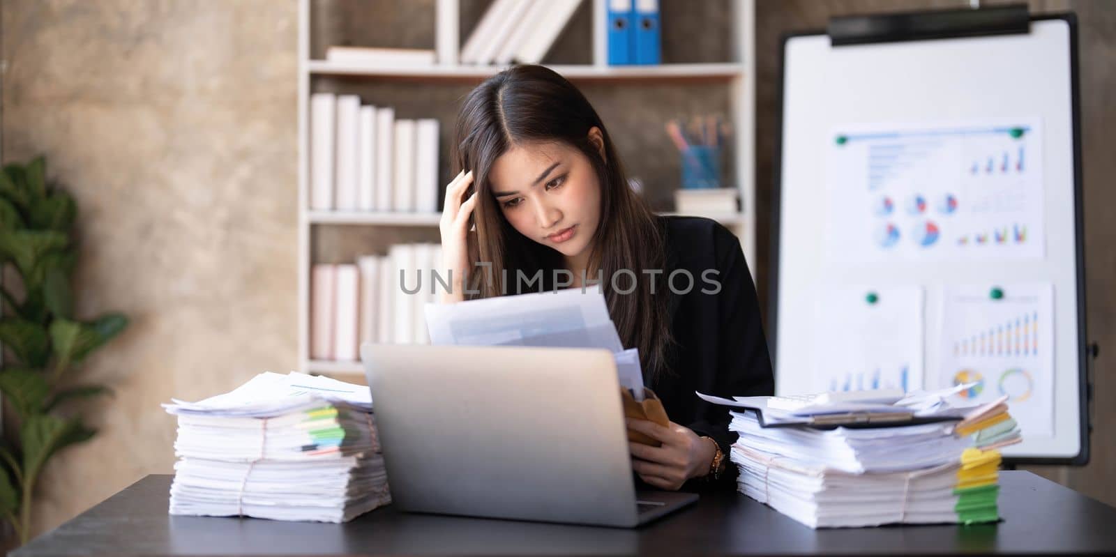 Young Asian businesswoman working on laptop computer, stressed has a headache and thinks hard from work at the office. by wichayada