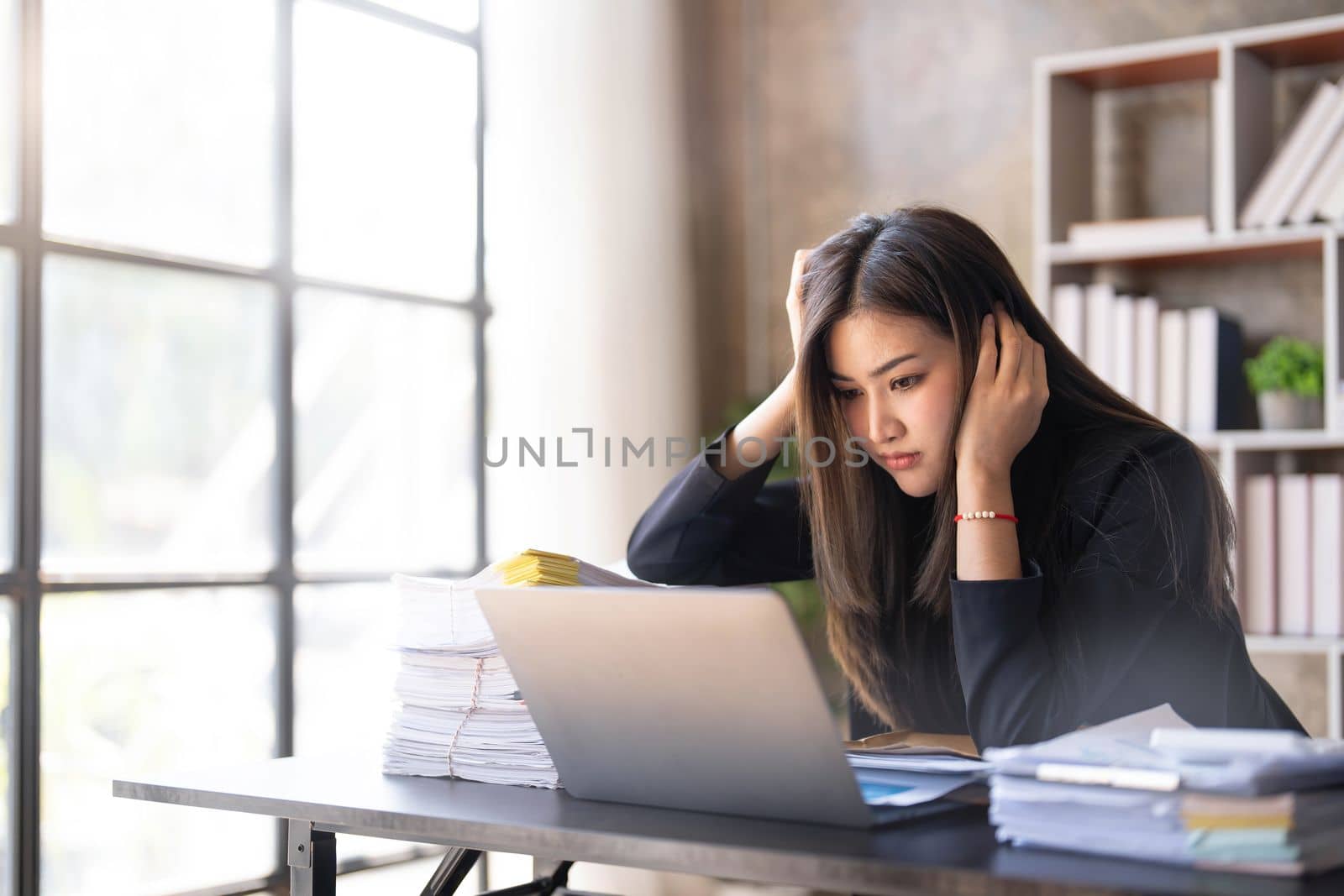 Young Asian businesswoman working on laptop computer, stressed has a headache and thinks hard from work at the office. by wichayada