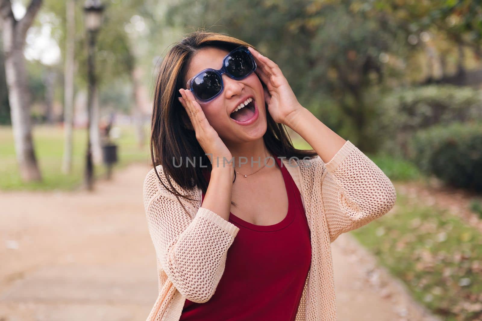 cheerful asian woman puts on her sunglasses laughing in the park, concept of youth and beauty