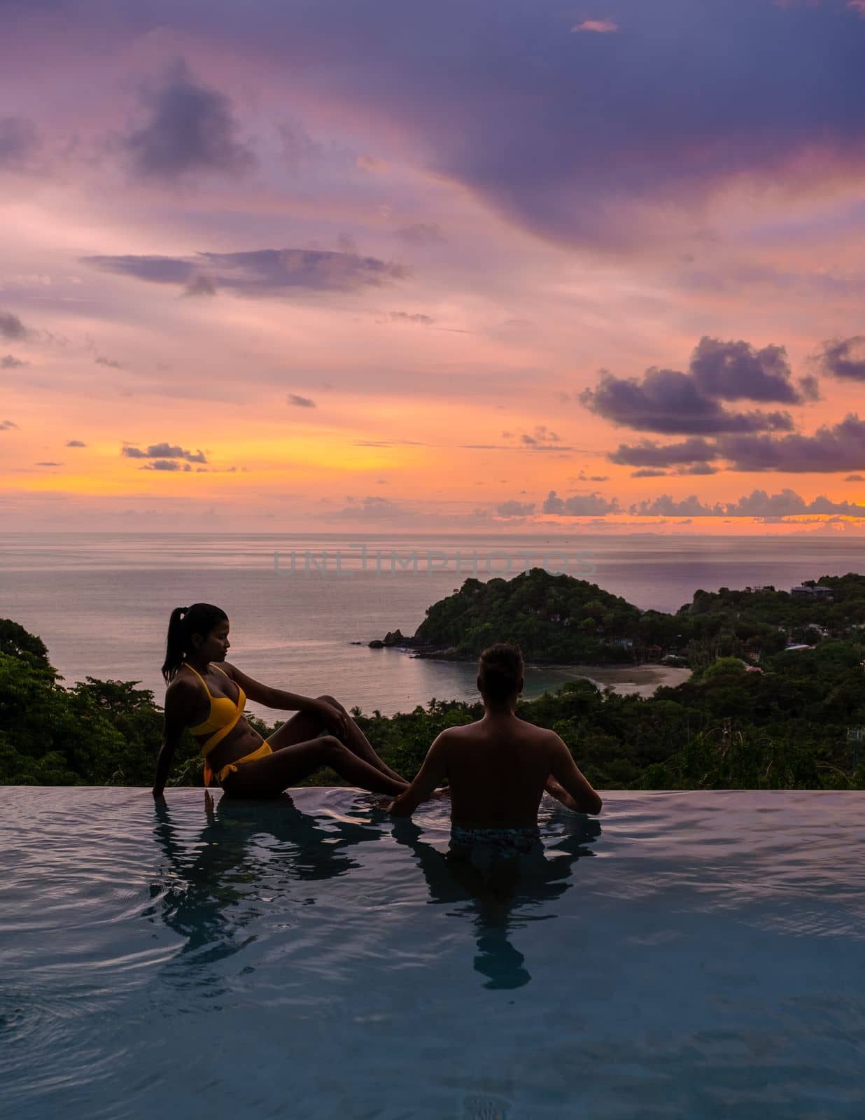 Romantic couple of men and women at a swimming pool during a vacation on a tropical island. man and woman in the infinity pool during sunset. luxury vacation in a luxury pool villa