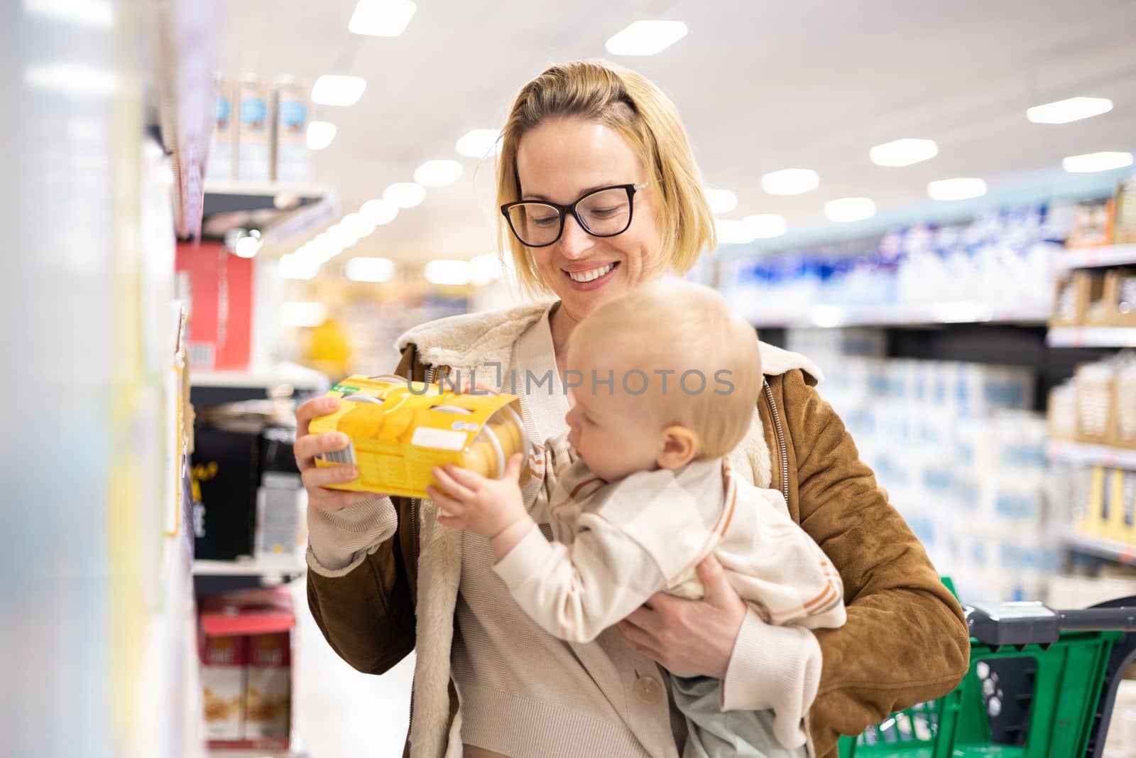 Caucasian mother shopping with her infant baby boy child choosing products in department of supermarket grocery store. by kasto