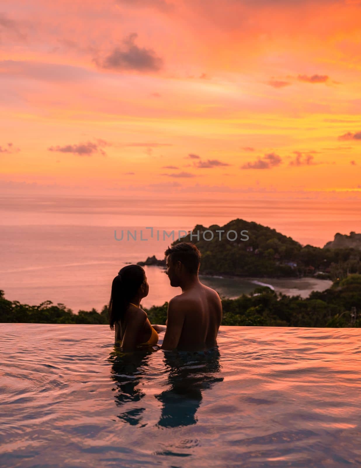 Romantic couple of men and women at a swimming pool during a vacation on a tropical island. man and woman in the infinity pool during sunset. luxury vacation in a luxury pool villa