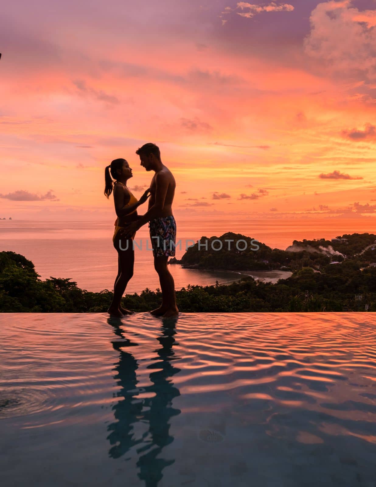 Romantic couple of men and women at a swimming pool during a vacation on a tropical island. man and woman in the infinity pool during sunset. luxury vacation in a luxury pool villa