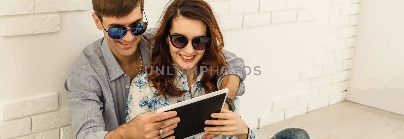 Happy couple with tablet, shopping online, making internet order sitting at home floor in empty living room