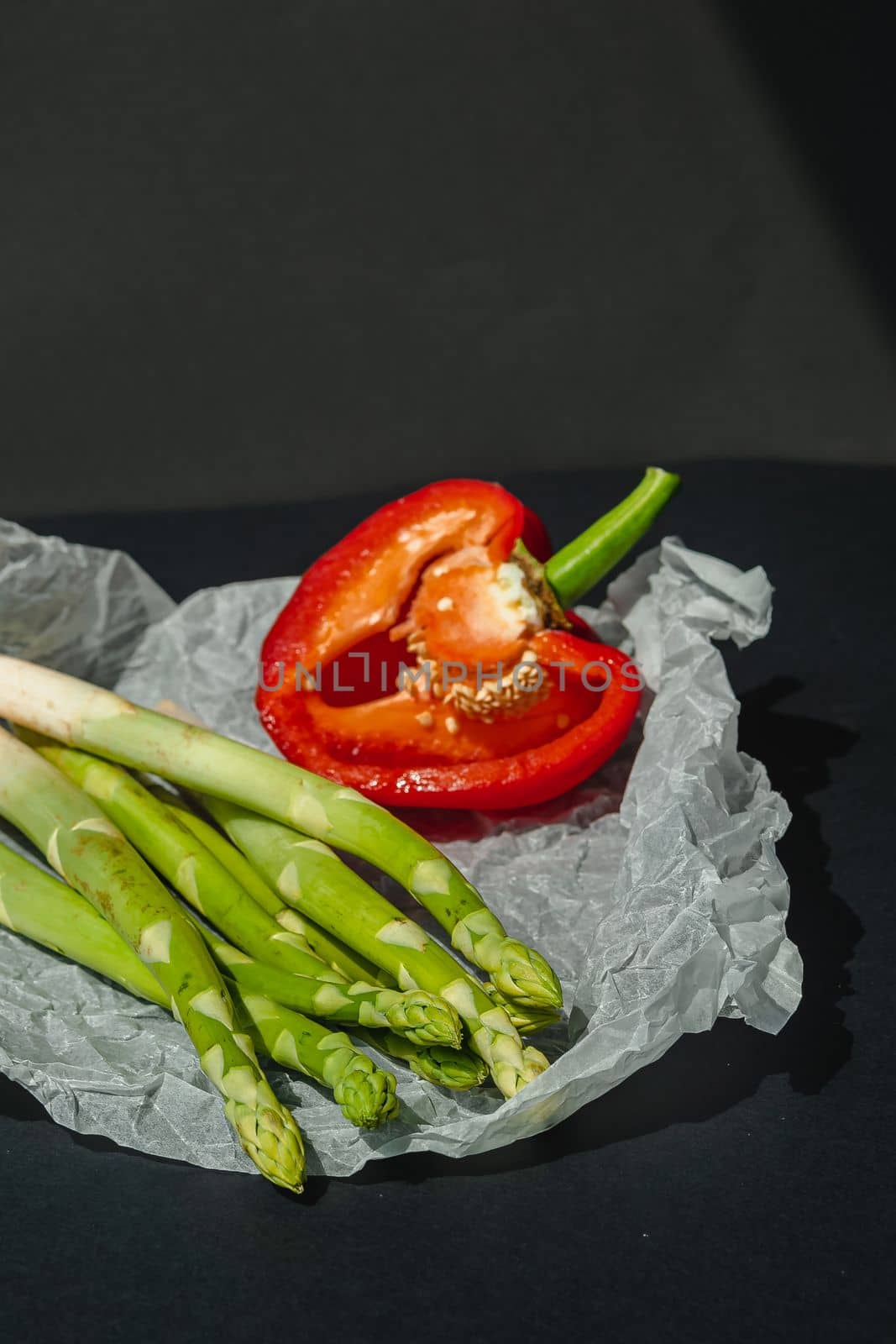 fresh green asparagus and half of red sweet, large pepper lie on white parchment on a dark gray background. proper nutrition. Lifestyle. place for text