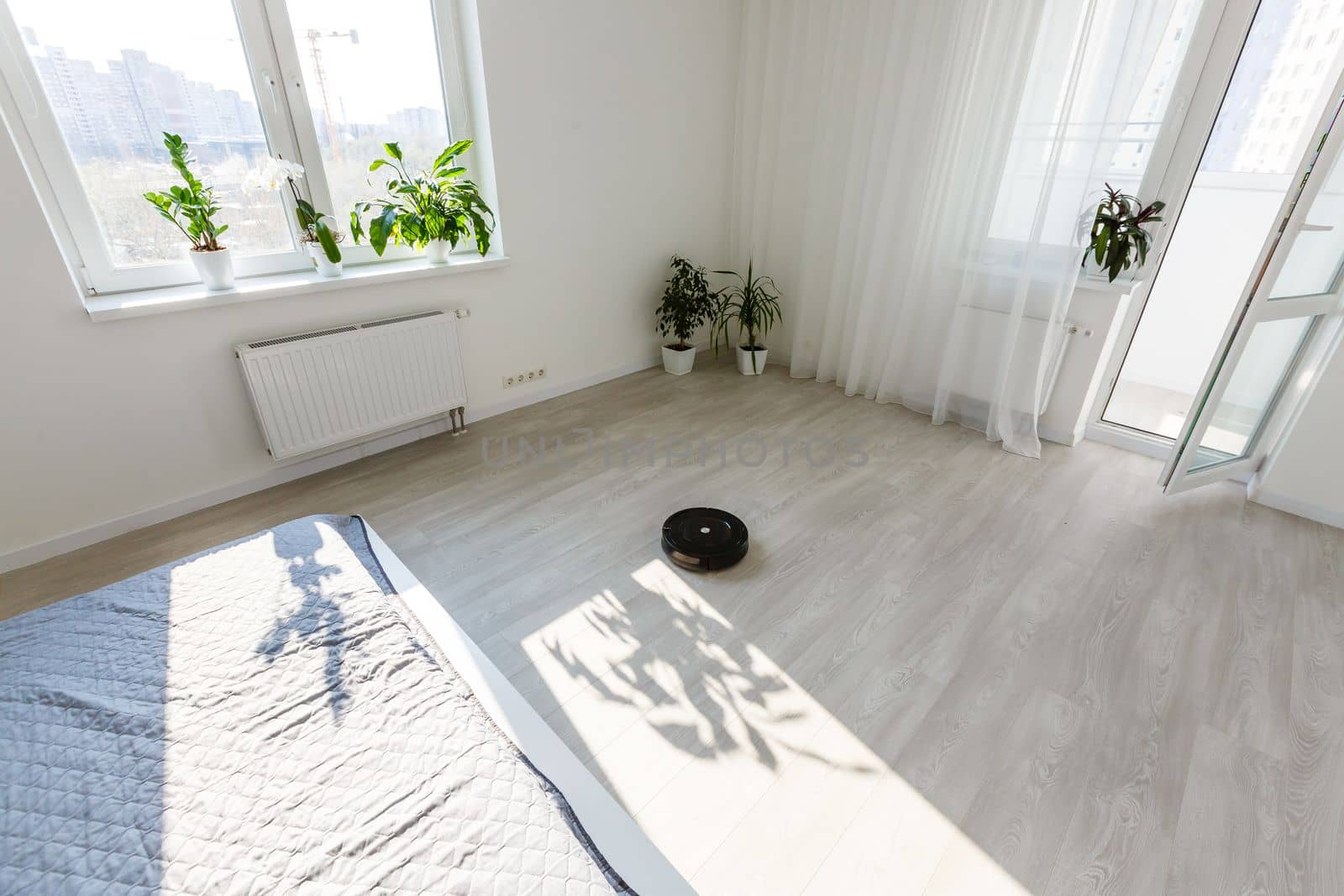 White robotic vacuum cleaner on laminate floor cleaning dust in empty room. Smart electronic housekeeping technology by Andelov13