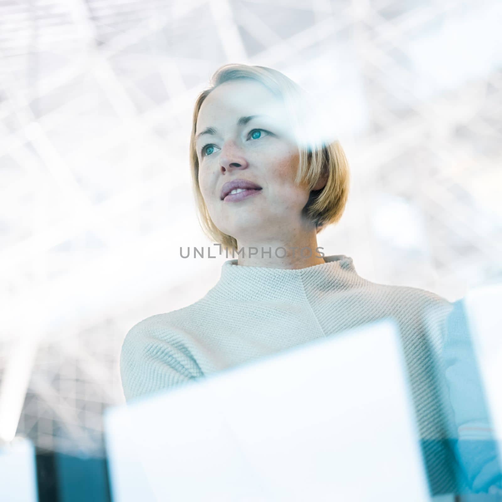 Portrait of strong, determined, successful young woman looking trough window while waiting to board an airplane at airport terminal departure gates. by kasto