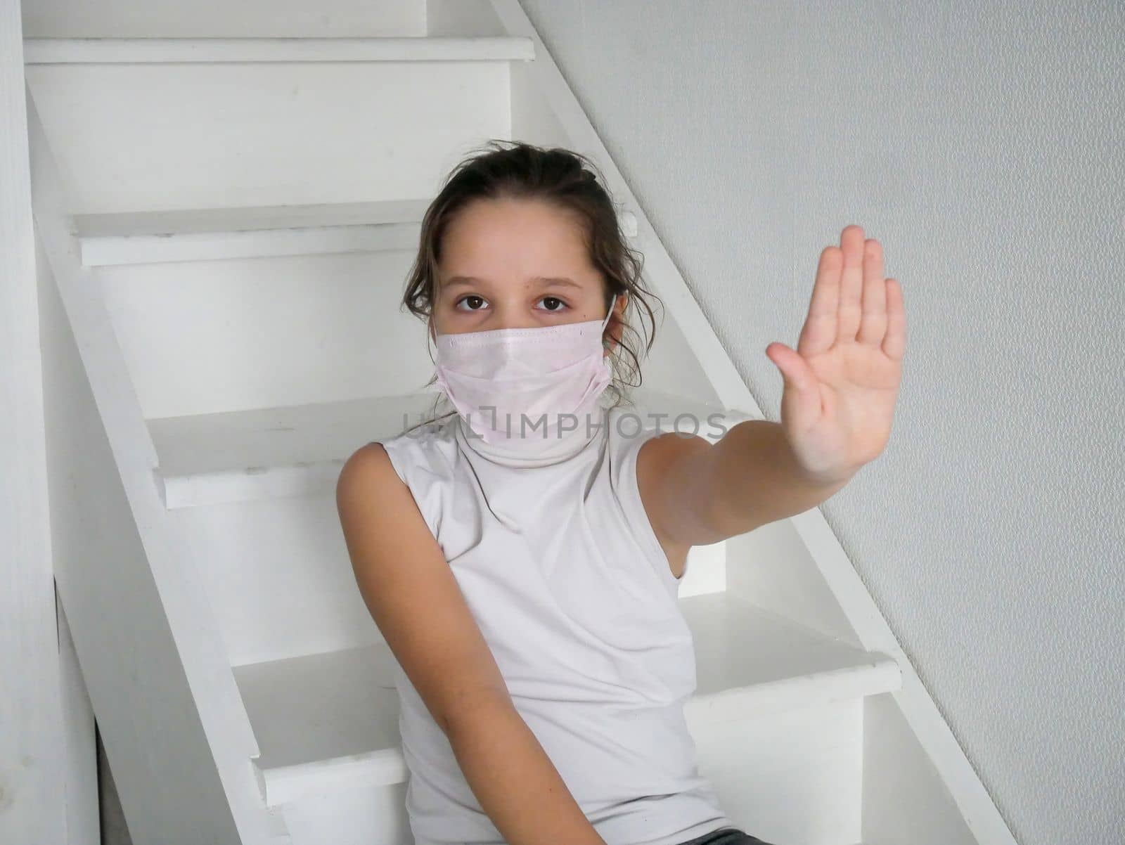 Little girl child in protective face mask showing hand stop sign on white background. Focus at his hand.