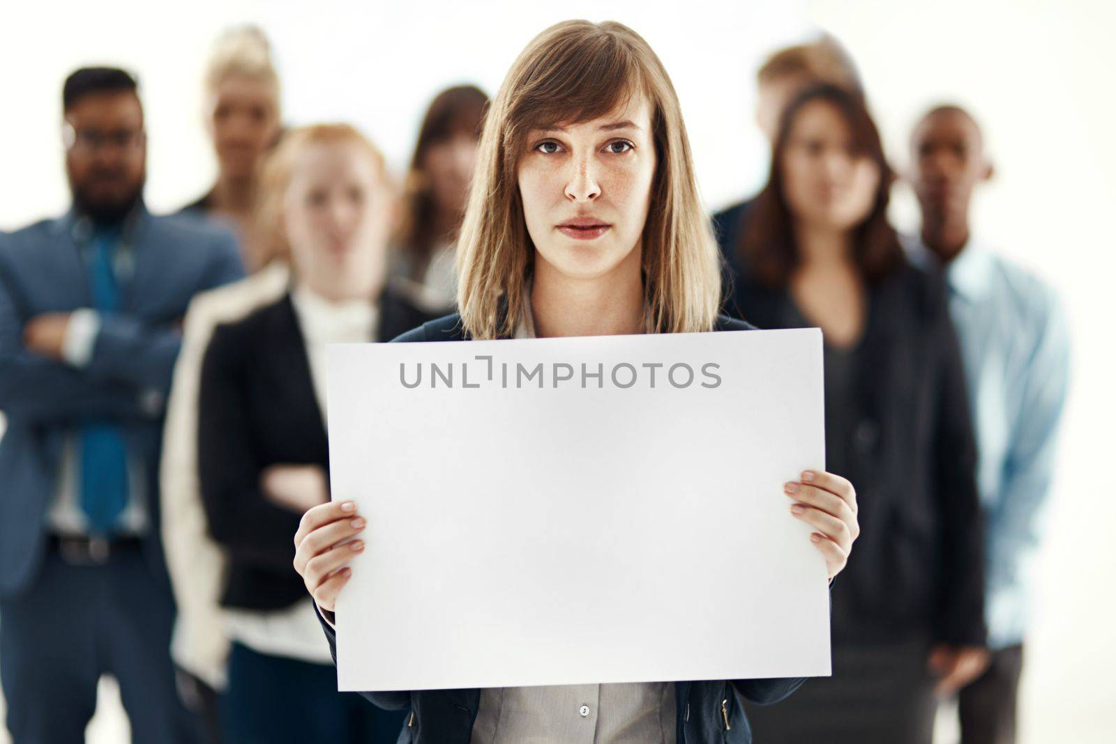 Supported by her team. Portrait of a young businesswoman holding a blank placard with her colleagues in the background