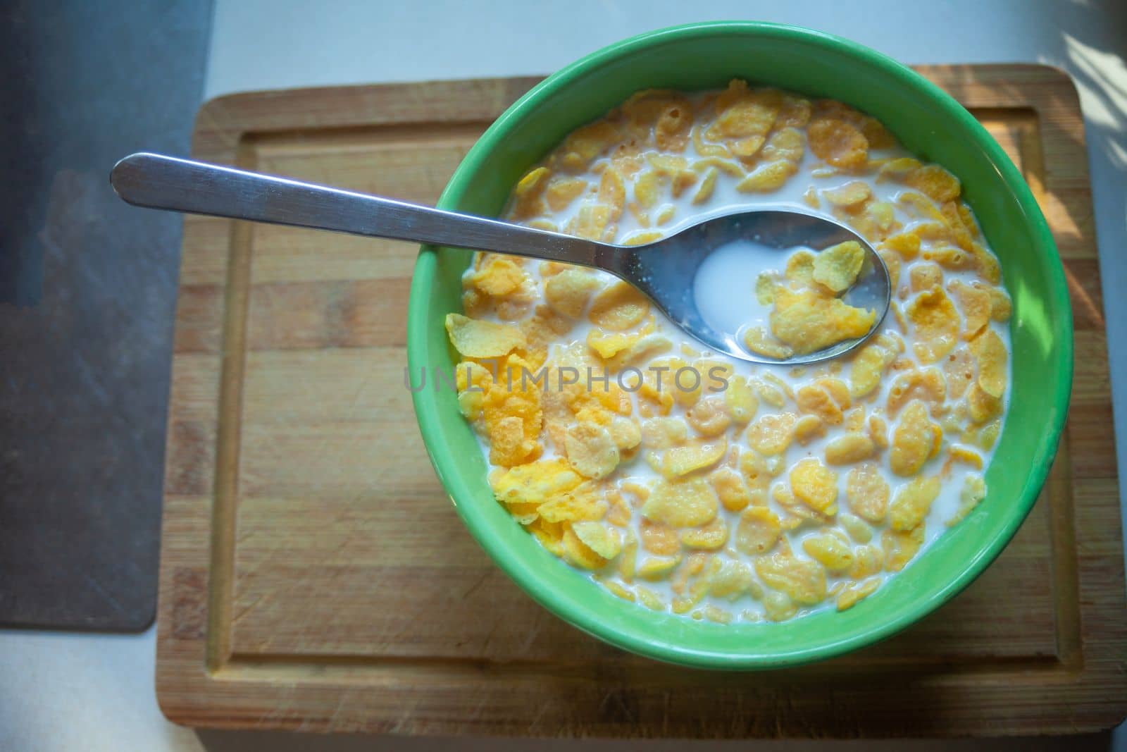 Corn flakes with milk in a green bowl with a spoon, top view