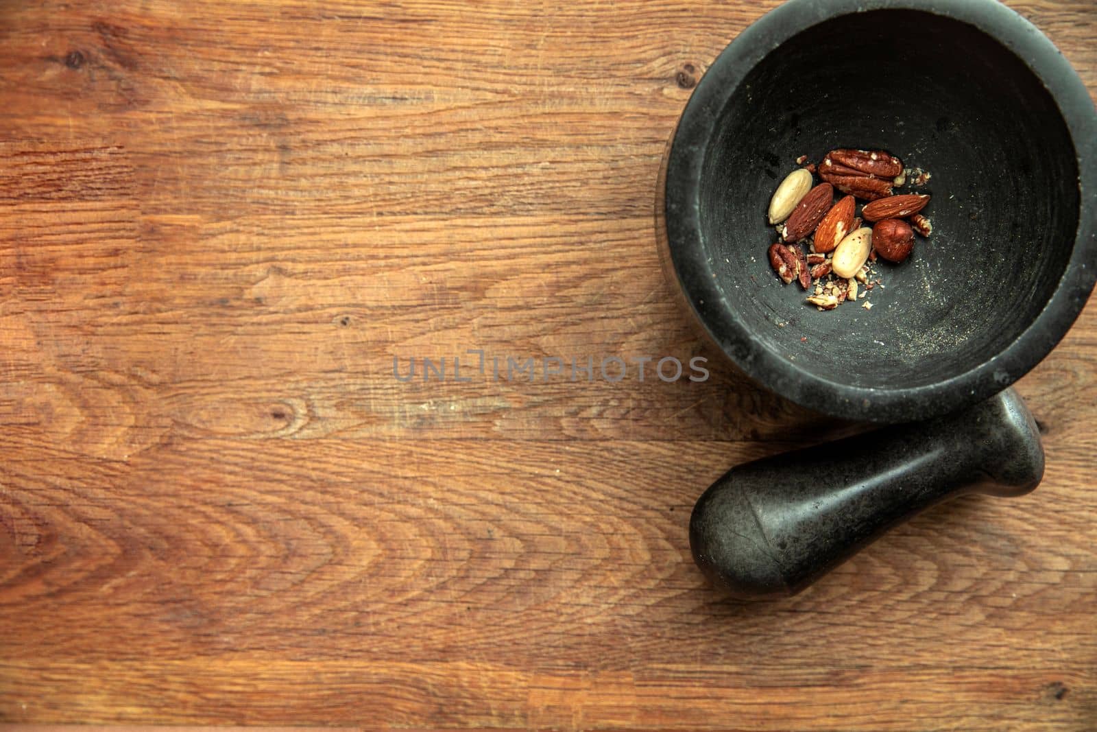 Top angle view of various nuts in stone mortar on a wooden shelf background, almonds, hazelnuts, walnuts dried top view and copy space healthy