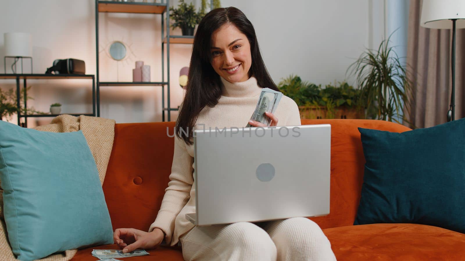 Planning budget. Rich happy young woman counting money cash use laptop computer calculate domestic bills at home room. Joyful girl satisfied of income earnings, saves money for planned vacation, gifts