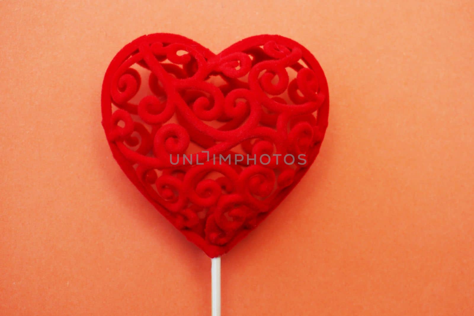 Valentine's Day concept. Copy space. Decorative red gift heart on a stick on an orange background.