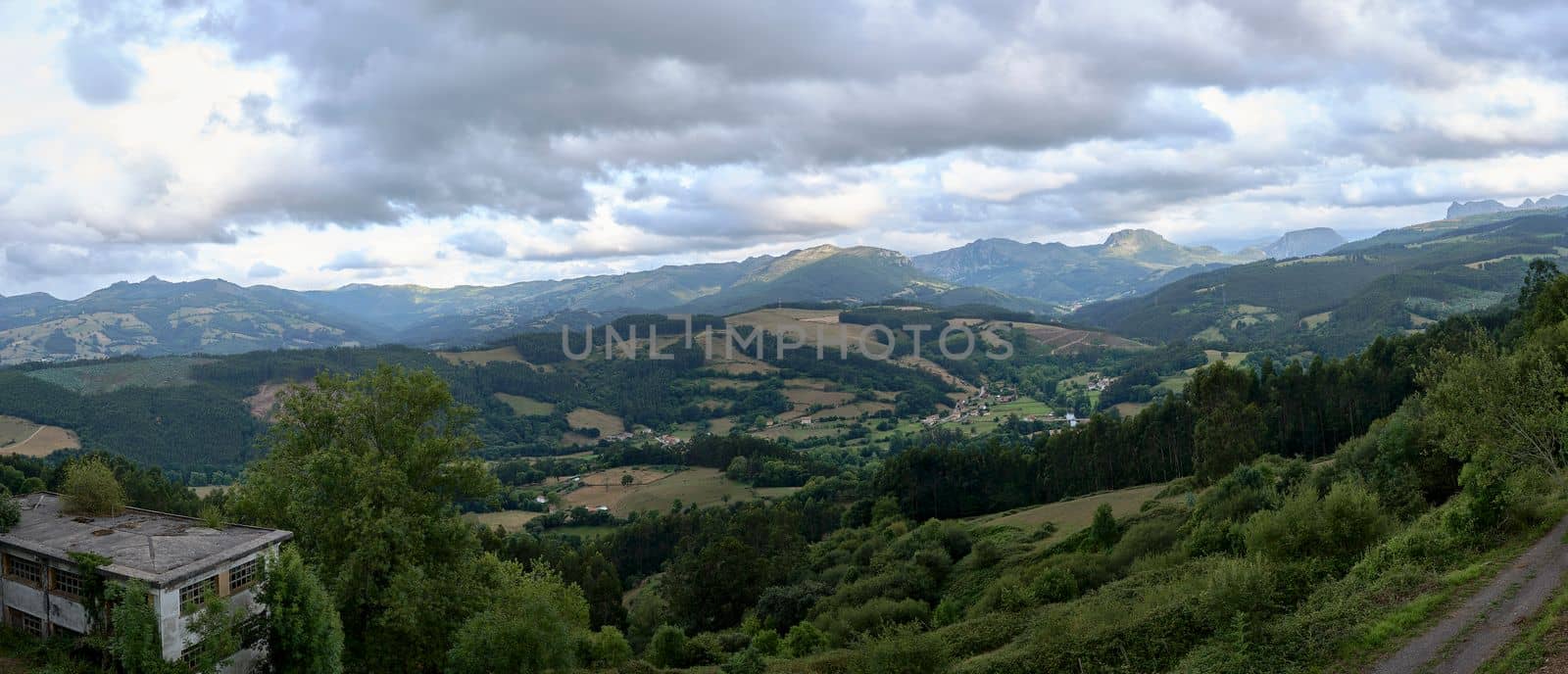 Rustic mountain landscape with cloudy sky.Bien Aparecida, Cantabria, meadows, trees and pastures for animals, rustic houses, sky with storm clouds.Panoramic photography