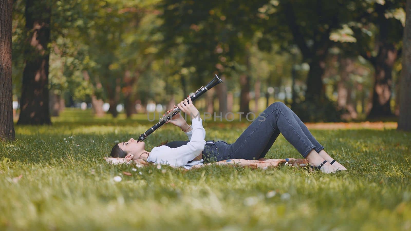 A girl plays the clarinet while lying on the grass in the park