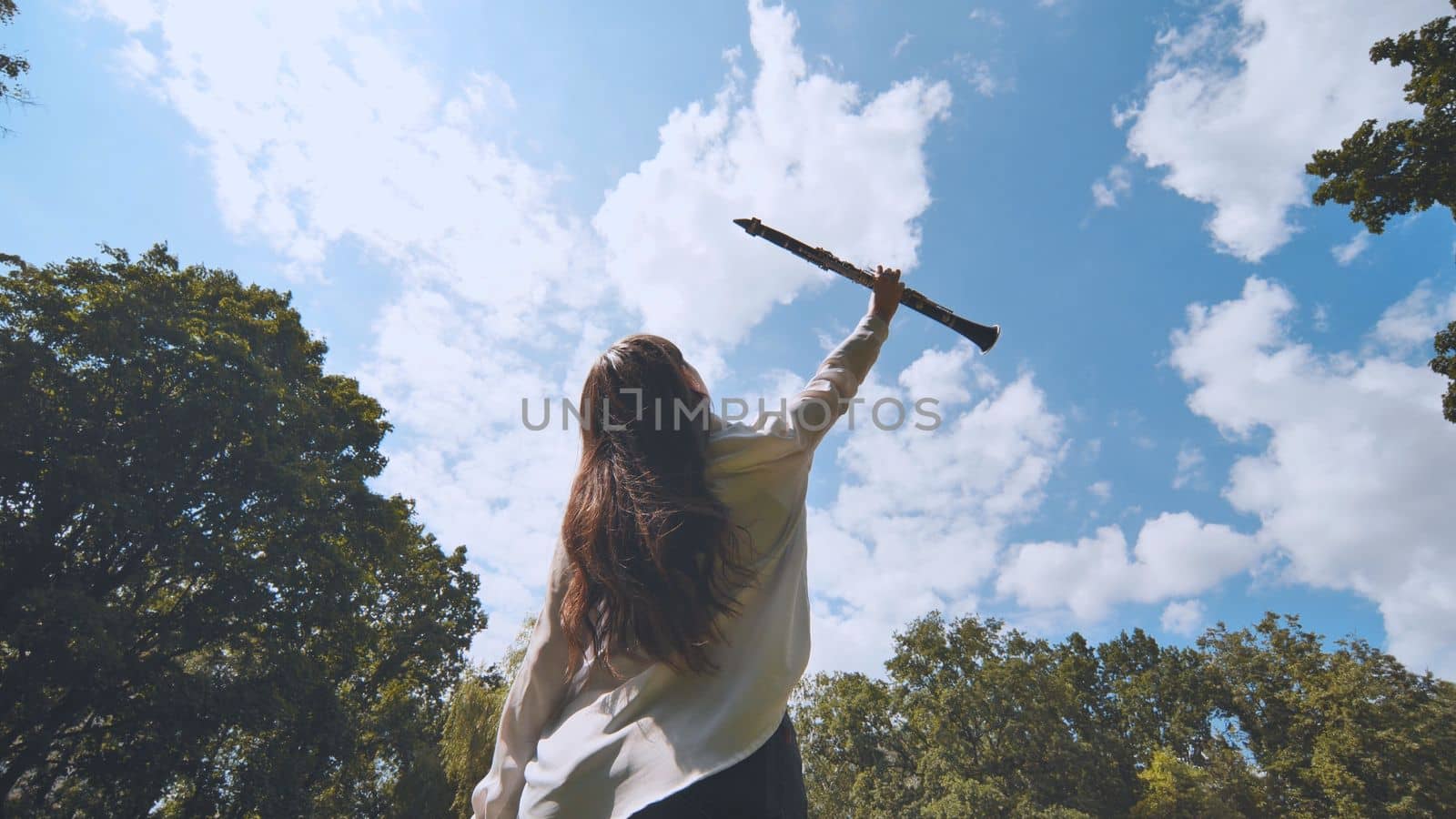 The inspired girl musician lifts the clarinet up against the blue sky