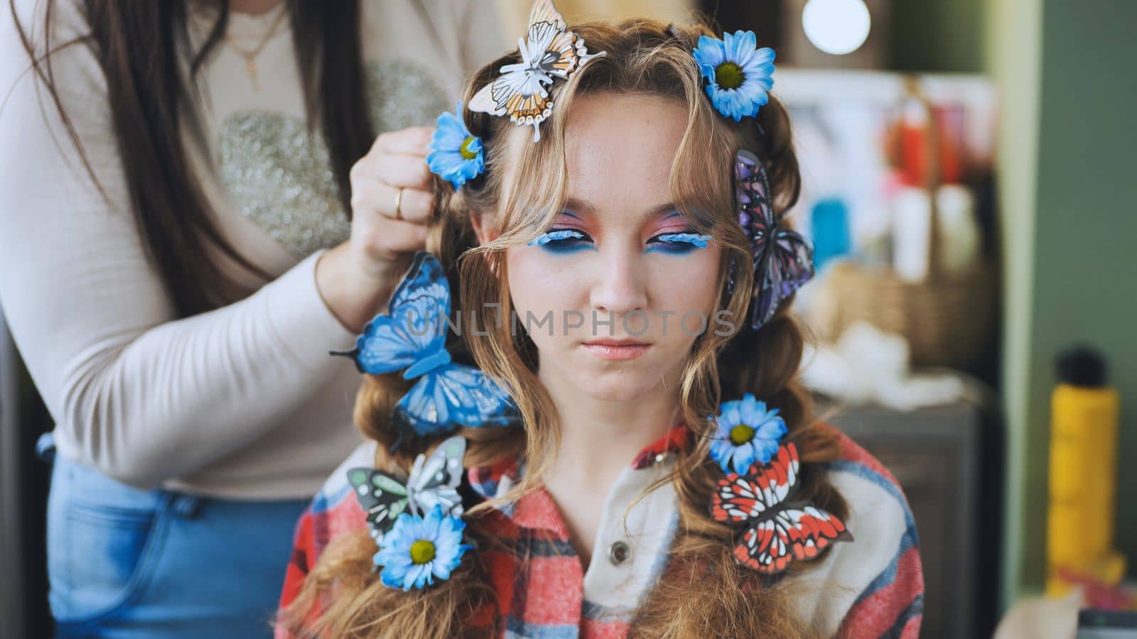 The hairdresser decorates the model's hair with blue flowers and butterflies